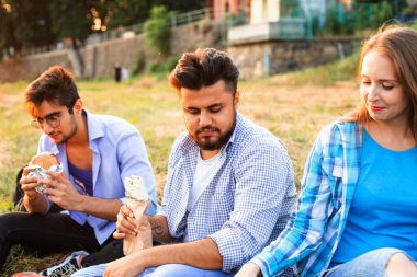 Genç çoklu etnik öğrenciler kampüste fast food yiyorlar.