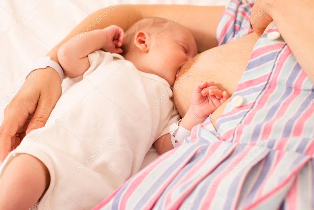 The mom is breastfeeding her newborn baby on the bed