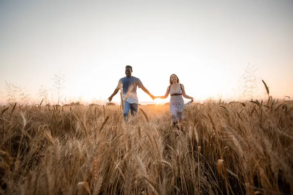 Gemischte Rasse junges erwachsenes Paar hält Händchen, während es auf dem Feld geht — Stockfoto