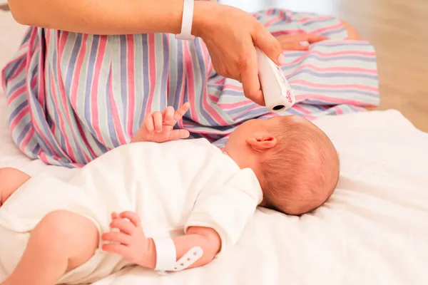 Mother measures newborn baby temperature on the bed — Stock Photo, Image