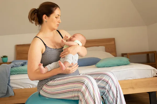 Mother holding and rocking baby sitting on fitball — Stock Photo, Image