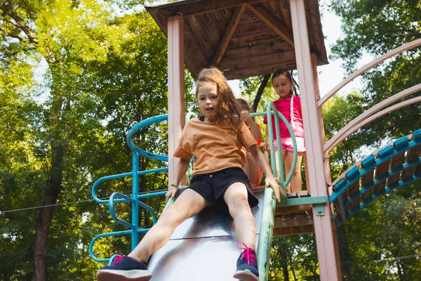 Het kleine meisje zit op een glijbaan in de speeltuin — Stockfoto