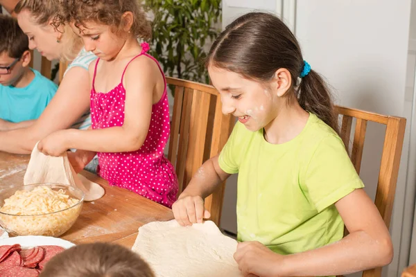 Crianças felizes sentam-se em uma mesa na cozinha e fazem pizza — Fotografia de Stock