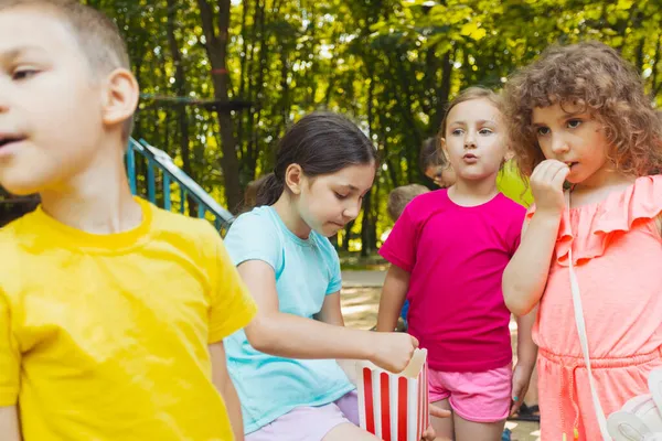 A gyerekek együtt esznek popcornt a parkban. — Stock Fotó