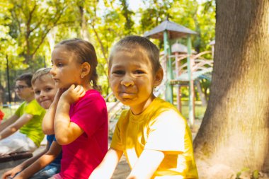 Mutlu çocuklar parkta bir bankta oturuyorlar.