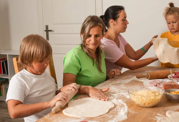 Dvě ženy středního věku s malými dětmi dělají pizzu — Stock fotografie