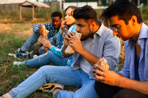 Den grupp unga olika människor som äter snabbmat på naturen — Stockfoto