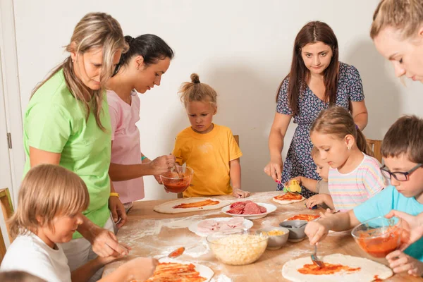 Группа матерей с детьми делают пиццу — стоковое фото
