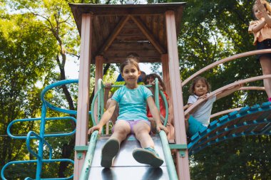 Küçük kız parkta bir kaydırağın üzerinde oturuyor.