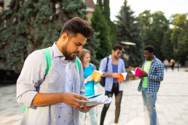 Hintli öğrenci dışarıda duruyor ve elinde bir yığın kitap tutuyor.