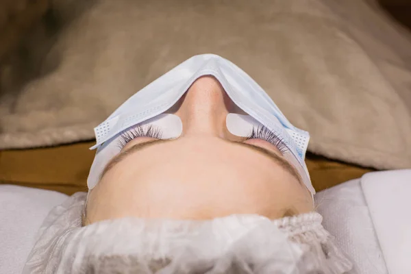 Wimper lamineren procedure close-up. Mooie vrouw met lange wimpers in een schoonheidssalon in geneeskunde masker — Stockfoto