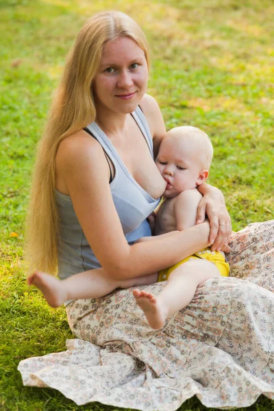 풀밭에 앉아 있는 아기에게 모유를 먹이는 어미 — 스톡 사진