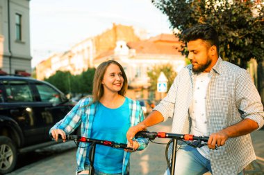 Sevgili çift elektrikli scooterlara biniyor ve birbirlerine bakıyorlar.