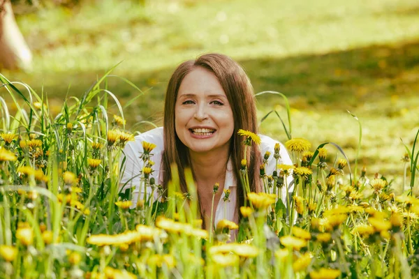 Lächelnde Frau liegt am Löwenzahnfeld — Stockfoto
