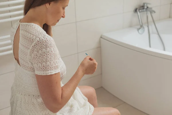 Medelålders kvinna med graviditetstest på toaletten — Stockfoto