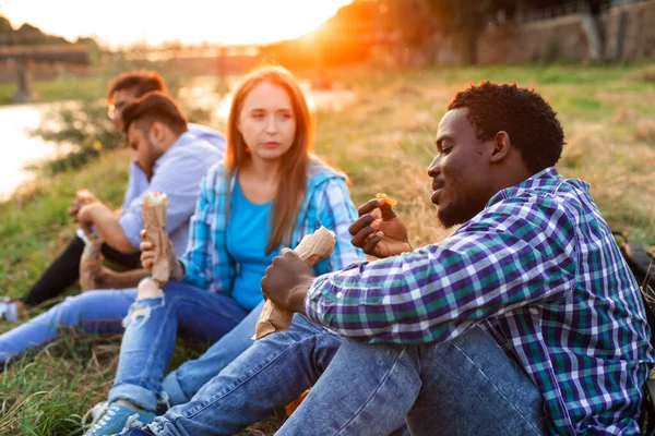 Den grupp unga olika människor som äter snabbmat på naturen — Stockfoto