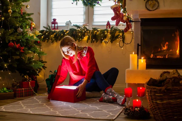 Woman open a red box gift near the fireplace — Stockfoto