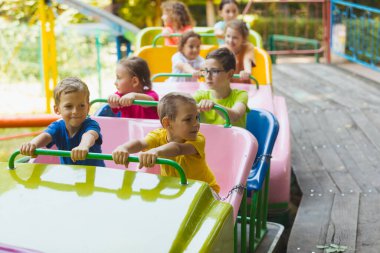 Mutlu küçük çocuklar güneşli bir günde lunaparktaki lunaparkta hız trenine binerler.