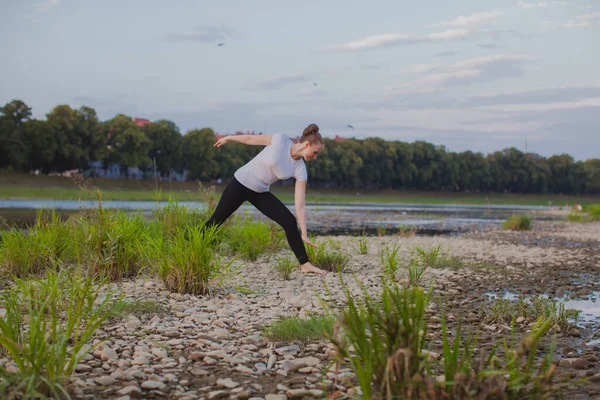 Yoga classes in nature. Young woman does yoga on rocks, near a river flows