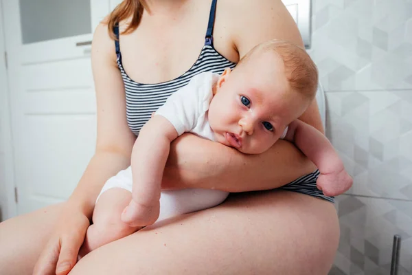 Tired depressed mother with crying newborn baby sitting on the lavatory pan