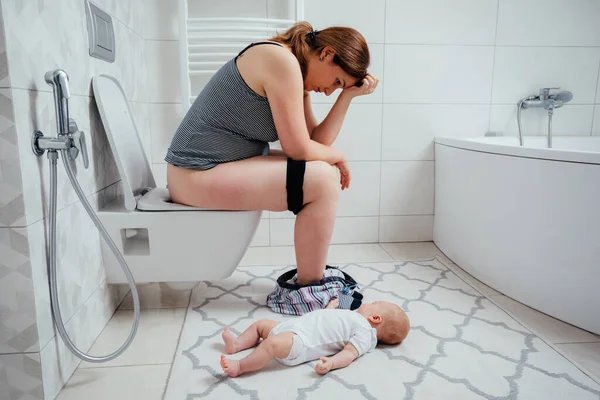 Tired depressed mother with crying newborn baby sitting on the lavatory pan