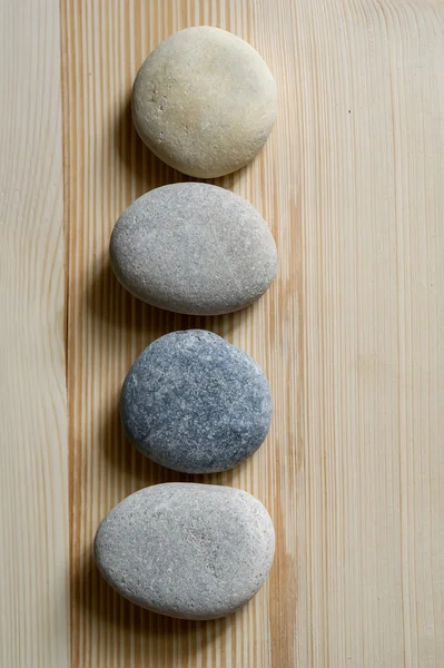 Cuatro piedras están alineadas en una línea sobre fondo de madera clara — Foto de Stock