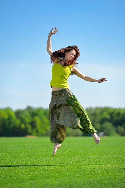 Junge Frau springt auf eine grüne Wiese — Stockfoto