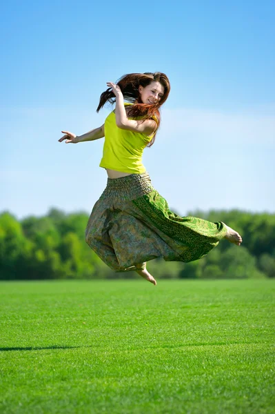 Junge Frau springt auf eine grüne Wiese — Stockfoto