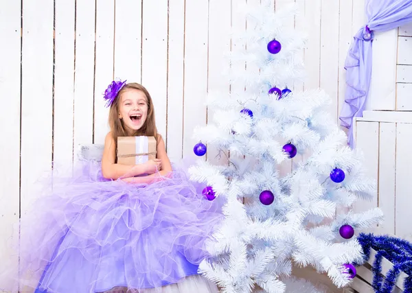 Little girl with a gift near Christmas tree — Stock Photo, Image