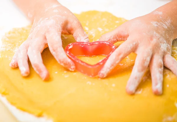 Little girl cuts dough in the shape of heart — Stock Photo, Image