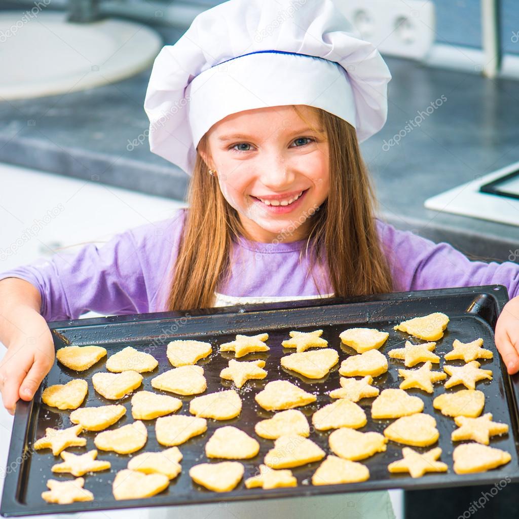 little girl holding a baking sheet of cookies