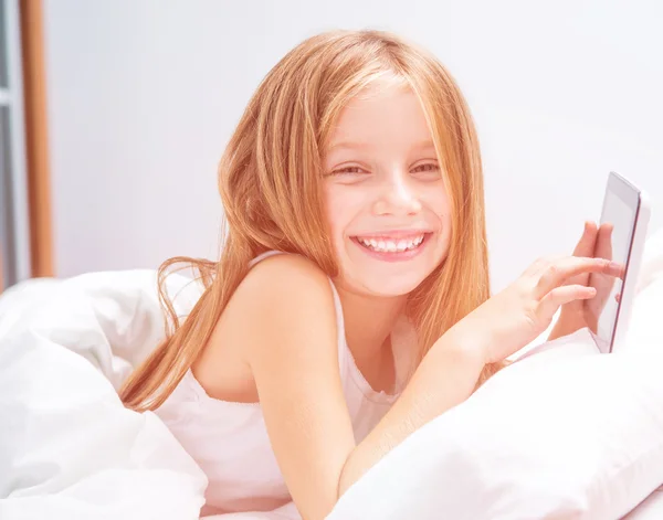 Schoolmeisje met tablet in bed — Stockfoto