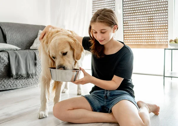 自宅で床に座って水でボウルを保持黄金の取得犬ときれいな女の子 美しいです女性ティーン人とともに飲む犬ペットで光の部屋 — ストック写真