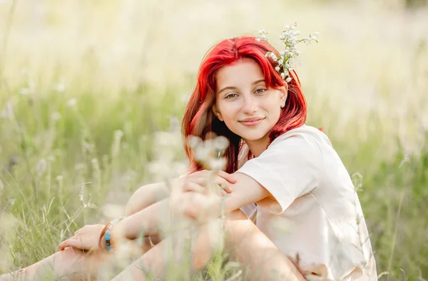 赤い髪の女の子は 自然と笑顔に座っている 日当たりの良いフィールドに花を持つかなり若い女性 — ストック写真