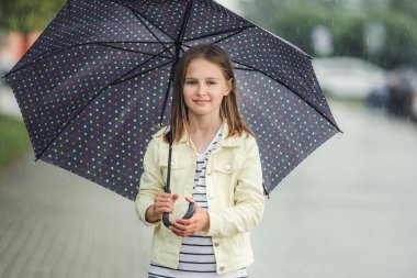 Yağmurlu bir günde dışarıda şemsiye altında güzel bir kız. Bulutlu, ıslak hava portresiyle şehirde yürüyen güzel bir çocuk.