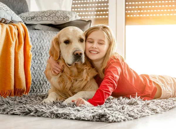 Golden retriever köpeği olan neşeli bir kız çocuğu kanepenin yanında yatıyor ve gülümseyen bir evcil hayvan. Saf labrador köpekli mutlu kız.