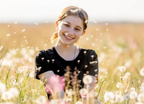 飛行タンポポと笑顔でフィールドに座っている可愛い女の子のティーンエイジャー 美しい若い女性モデルに自然で晴れた日の肖像画 — ストック写真