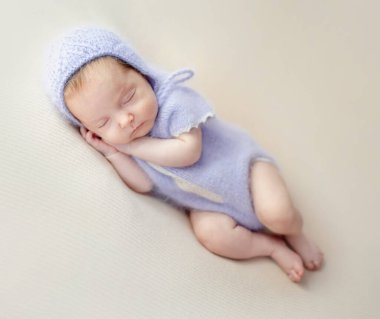Newborn baby girl wearing knitted costume and wreath lying on pillow. Cute infant child kid istudio photoshoot