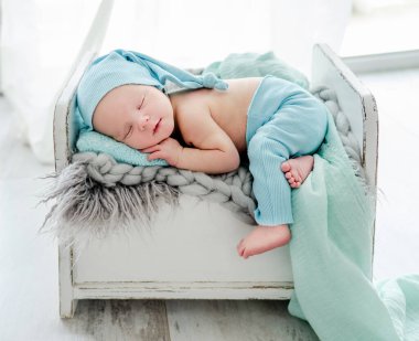 Newborn baby child sleeping on tiny bed on his tommy and wearing knitted pants and hat. Sweet infant kid napping on fur