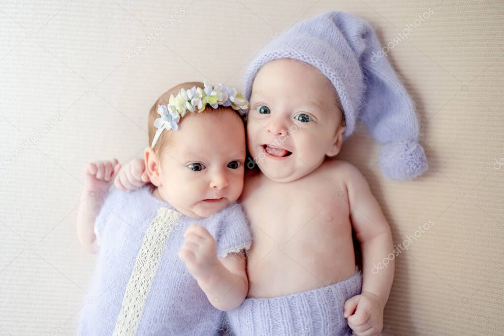 Newborn babies twins wearing knitted costumes lying together and looking at camera. Cute infant child kids brother and sister studio photoshoot
