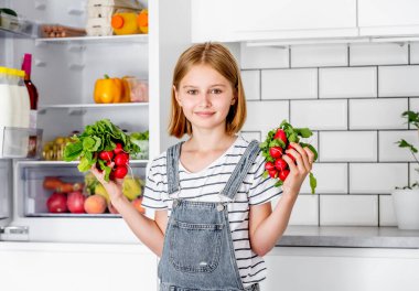Preteen girl with red radish at kitchen posing and smiling. Pretty child with fresh vitamin vegetables at home