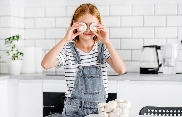Preteen girl with champignons posing at kitchen. Pretty child with mushrooms food at home