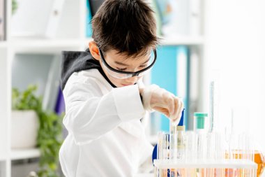 Korunma gözlüğü takan okul çocuğu ilkokul fen dersinde kimya deneyi yapıyor ve bileşenleri karıştırıyor. Test sırasında laboratuvarda zeki bir öğrenci.