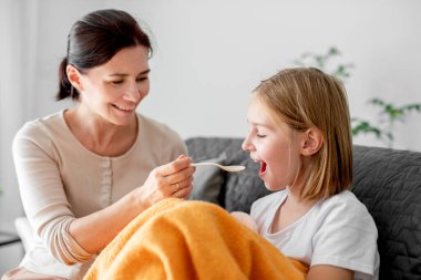 Anne hasta çocuğa evde ilaç şurubu veriyor. Anne kadın ateşi ve virüsü olan çocuğu önemsiyor.