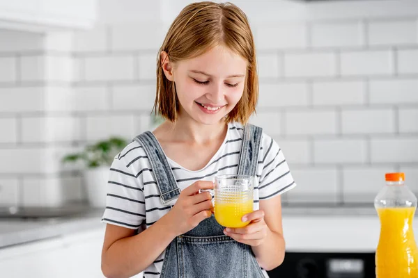 キッチンで笑っているガラスの中にオレンジジュースを持つ18人の女の子 ビタミンフルーツドリンク付きの可愛い子供は家で幸せ — ストック写真