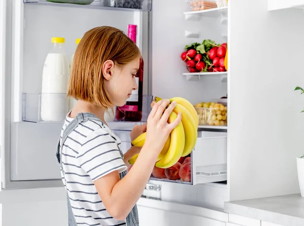 有香蕉的少女在厨房里看着冰箱里的维生素健康食品 漂亮的孩子在家里带着黄色的水果 — 图库照片