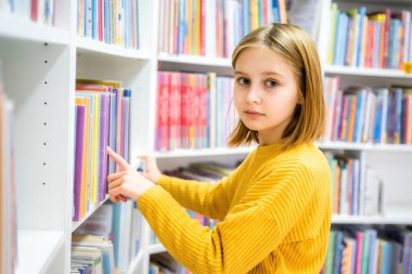 Okul kütüphanesinde kitap seçen liseli kız. Okumak için edebiyat seçen zeki bir kız. Kitapçıdaki raflardaki kitaplar. Kitaplardan öğreniyorum. Okul eğitimi. Günlük okumanın faydaları