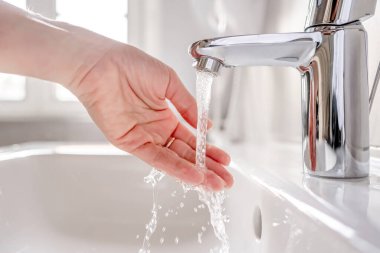 Genç bir kadın banyodaki lavabonun üzerinde ellerini sabunla yıkıyor..