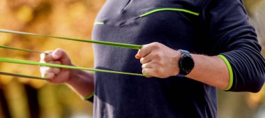 Stadyumda elastik lastikle antrenman yapan güçlü bir adam. Kollar ve göğüs egzersizi sırasında spor malzemesi olan yetişkin bir erkek. Sporcu dışarıda egzersiz yapıyor.