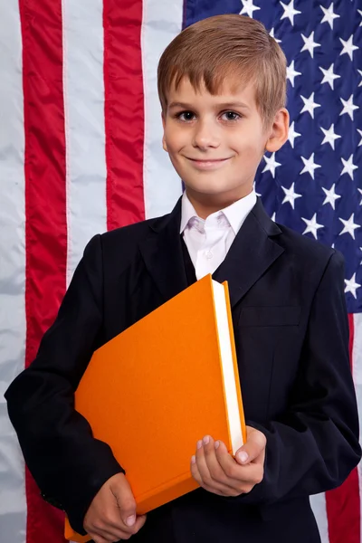 Netter Schuljunge hält ein Buch gegen die US-Flagge — Stockfoto